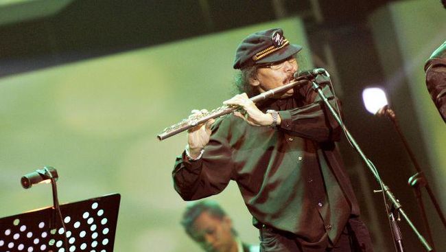 Benny Likumahuwa mengenakan pakaian serba hitam dan topi memainkan flute